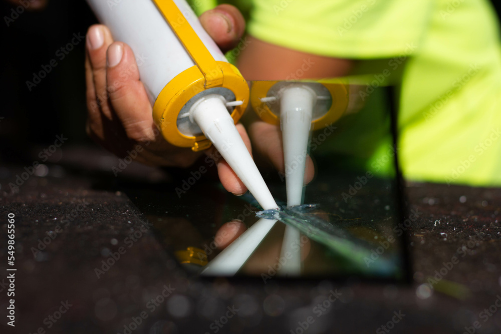 The craftsman's hand uses a silicone adhesive to connect the glass to