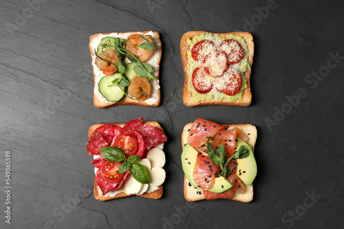 Tasty toasts with different toppings on black table, flat lay photo