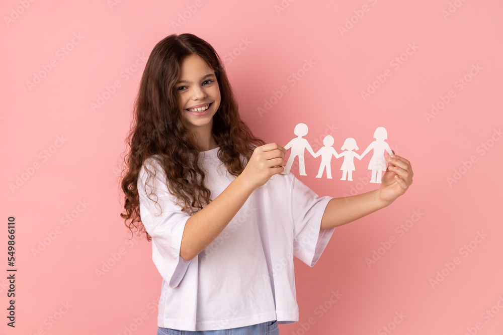 Portrait of smiling charming little girl wearing white T-shirt holding paper chain people in hands, happy family, relationships, childhood. Indoor studio shot isolated on pink background. Portrait of smiling charming little girl wearing white T-shirt holding paper chain people in hands, happy family, relationships, childhood. Indoor studio shot isolated on pink background.