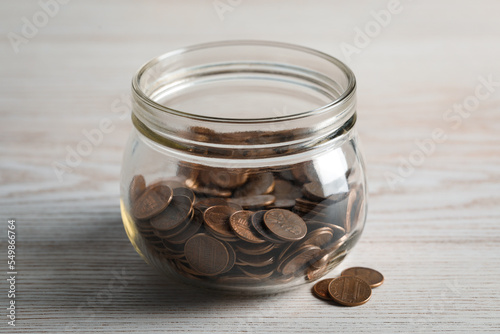 Glass jar with coins on white wooden table, closeup