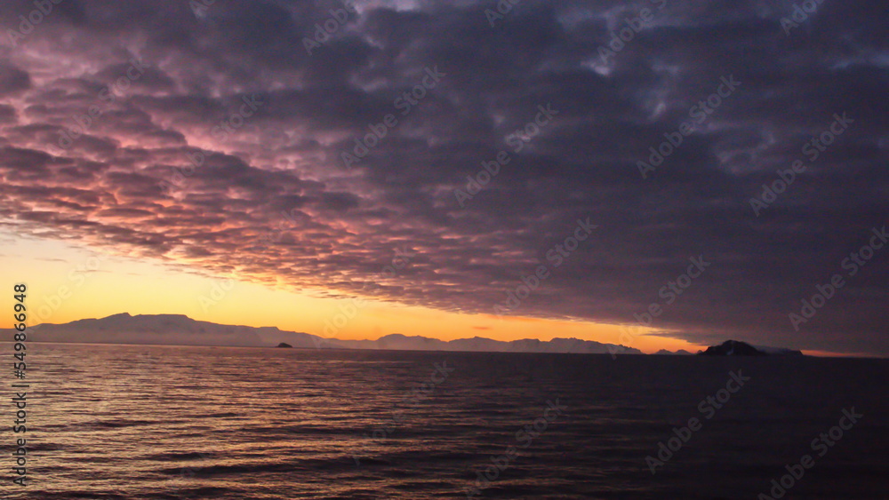 Popcorn clouds illuminated pink over the silhouette of a mountain, at sunset at Cierva Cove, Antarctica