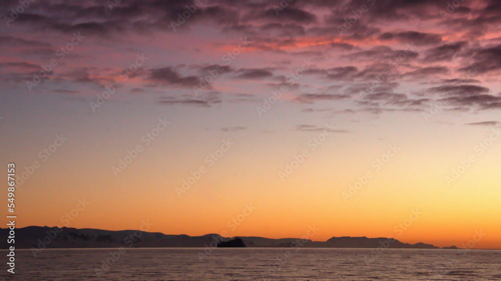 Naklejka premium Popcorn clouds illuminated pink over the silhouette of a mountain, at sunset at Cierva Cove, Antarctica