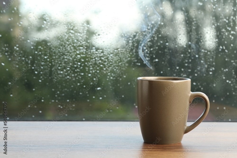 Cup of hot drink near window on rainy day. Space for text