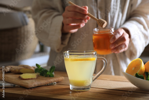 Woman making aromatic ginger tea at wooden table indoors, closeup