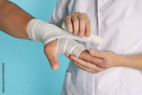 Doctor applying bandage onto patient's hand on light blue background, closeup