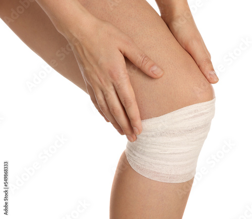 Woman with knee wrapped in medical bandage on white background, closeup
