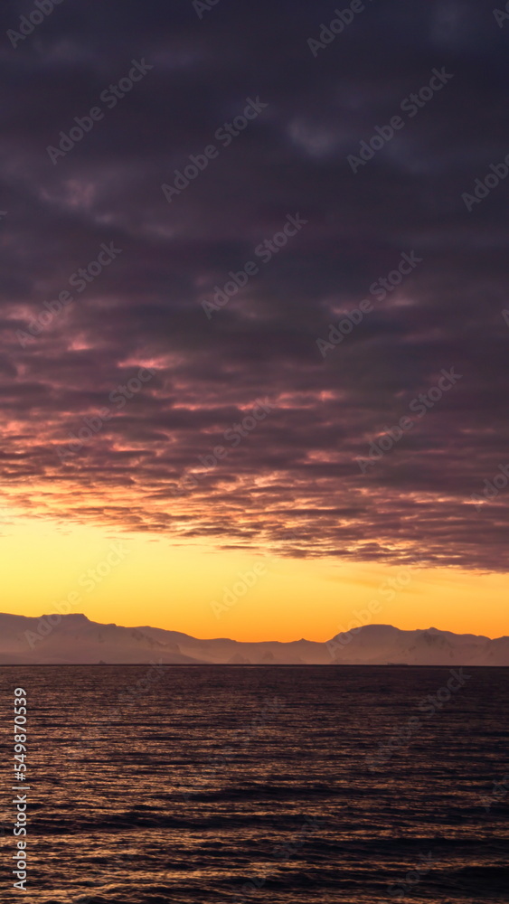 Popcorn clouds illuminated pink over the silhouette of a mountain, at sunset at Cierva Cove, Antarctica