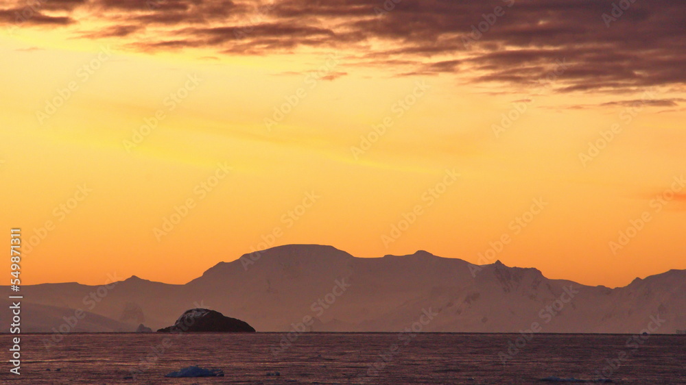 Popcorn clouds illuminated pink over the silhouette of a mountain, at sunset at Cierva Cove, Antarctica