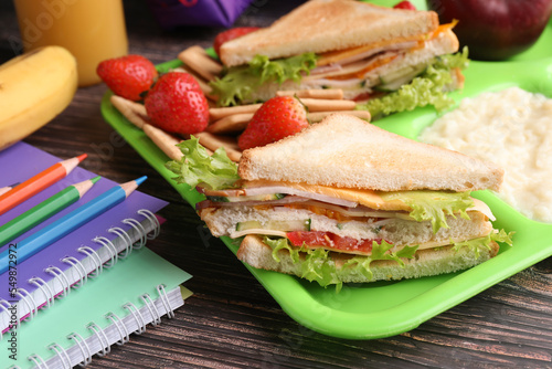 Serving tray of healthy food and stationery on wooden table, closeup. School lunch