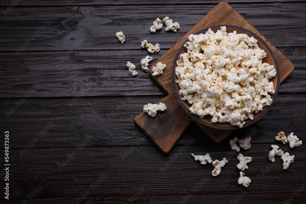 Tasty popcorn on black wooden table, flat lay. Space for text