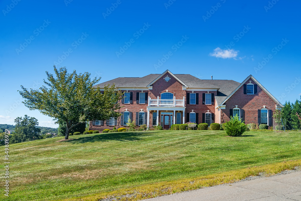 Large traditional American single family home with beautiful landscaping and lawn. Summer landscape on a sunny day under a blue sky.