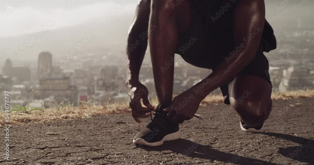 Running, road and black man feet while tying shoes for exercise, workout and cardio training outdoor on asphalt with city background. Athlete fastening sneakers laces outdoor for run in South Africa