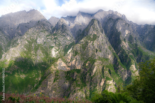 Beautiful horzontal panorama view of Jade Dragon snow mountain from hiking trail path of Tiger Leaping Gorge with blue sky in background, is located in Lijiang city, Yunnan, China