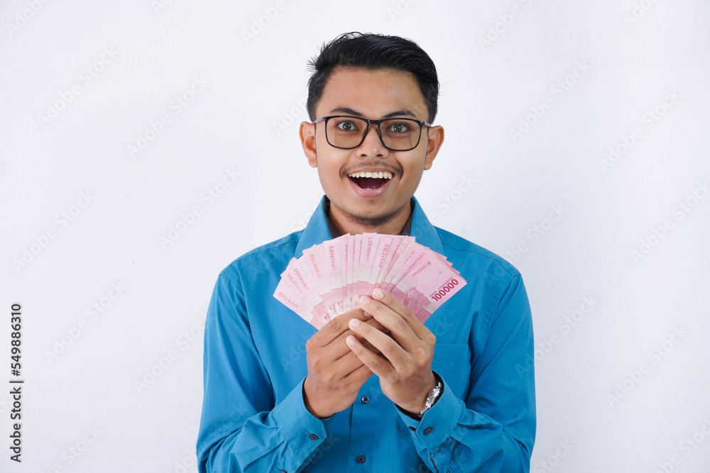 surprised or shocked handsome young asian businessman in wearing blue shirt and glasses holding fan of indonesia banknotes in hands isolated on white background surprised or shocked handsome young asian businessman in wearing blue shirt and glasses holding fan of indonesia banknotes in hands isolated on white background