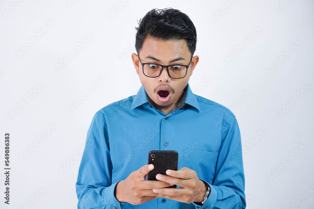 Portrait of surprised and shocked handsome young asian businessman with glasses in wearing blue shirt using smartphone isolated on white background Portrait of surprised and shocked handsome young asian businessman with glasses in wearing blue shirt using smartphone isolated on white background