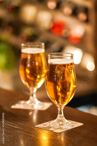 Two pints of lager beer standing on the bar table from a pub with bubbles coming out of the glasses. Photo with a scene from a bar. Beer beverages industry.