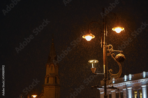 Concept photo for winter. Photo with a cinematic fairytale calm snowfall falling over a vintage looking street lamp with warm light. 