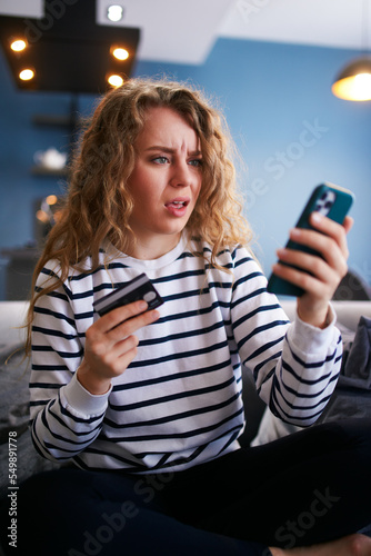 Worried woman with smartphone, debit card has problem paying bill, forgot banking app password. Female can't pay due to insufficient funds, sanctions, unsecure transfer. Unsuccessful transaction. photo