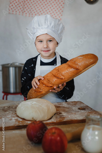 a little boy in a chef's cap and apron in the kitchen with a loaf