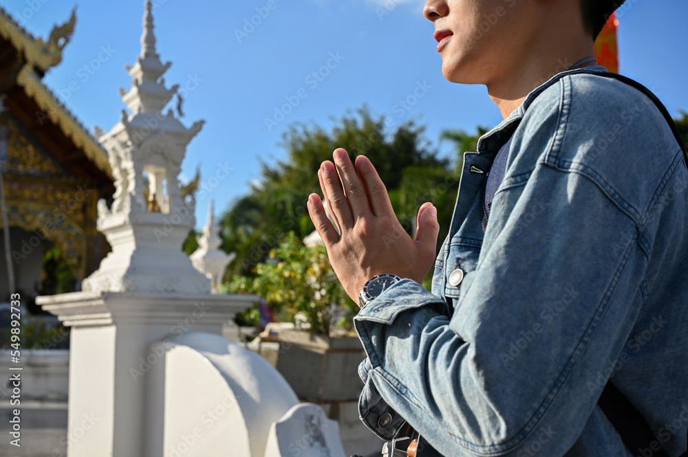 Fototapeta premium Handsome Asian male tourist putting his hands together in a prayer position at the temple. cropped