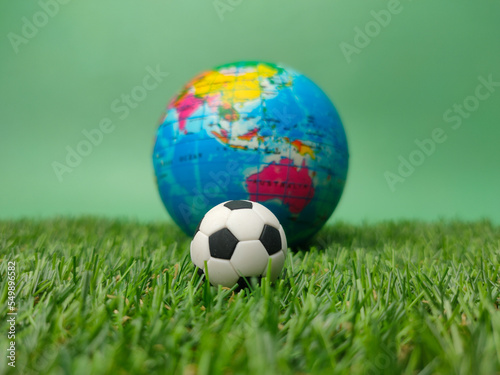 A ball is on a green field with a blurred globe behind it.