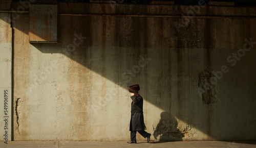 a hasidic jewish man walking down the street under the bridge in williamsburg brooklyn