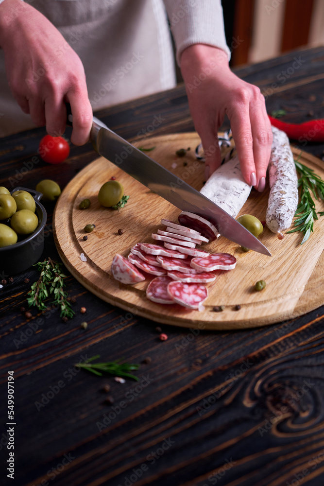 Woman slicing Spanish fuet salami sausageon wooden cutting board at domestic kitchen