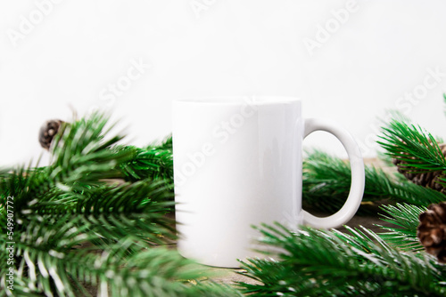White cup with empty copy space on a white background with green Christmas tree branches. Template for applying text and drawing, front view.