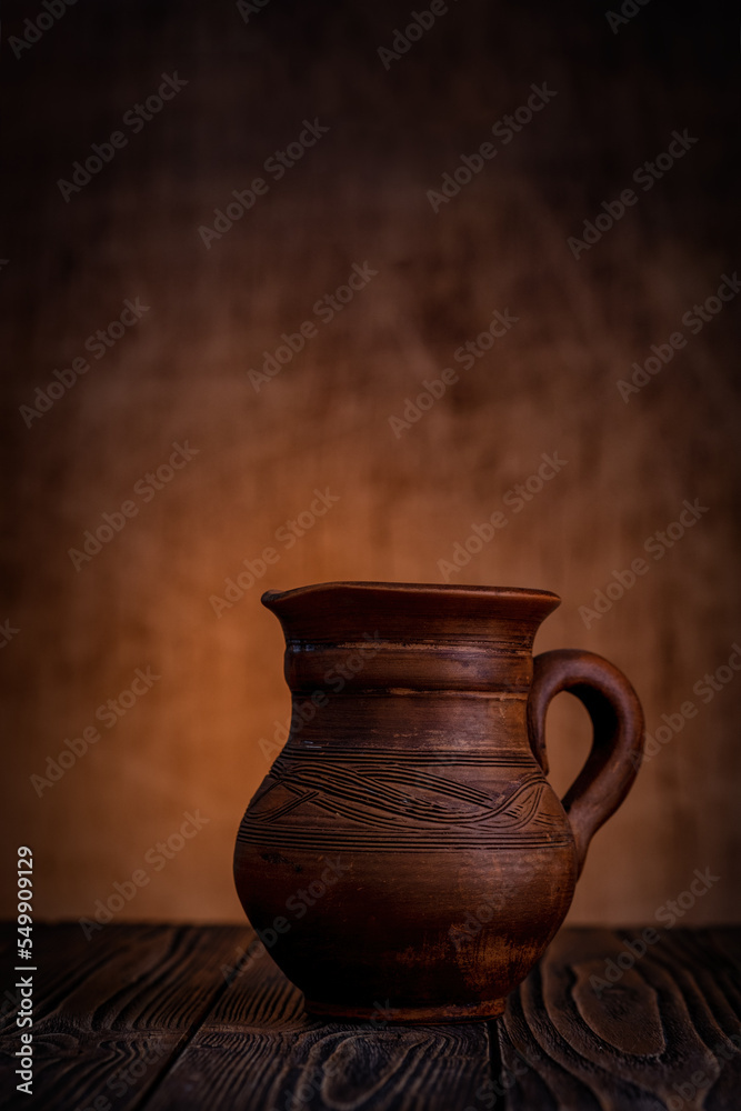 Clay jug on a dark background on a wooden table.