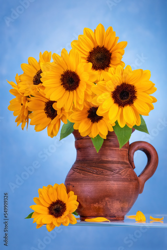 Clay jug with sunflowers on a blue background on glass.