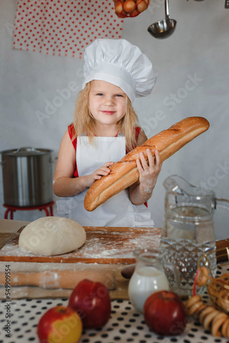 a little girl in the kitchen in a chef's cap with a baguette in her hands
