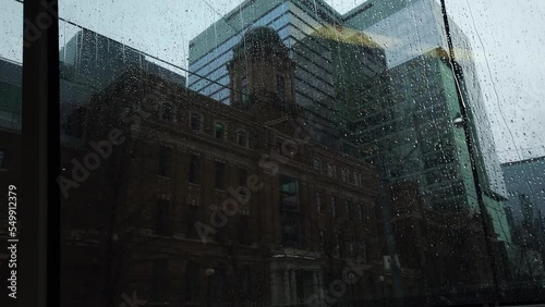 Travelling passenger point of view looking out the back end of a streetcar through a rain soaked window at city buildings going by photo