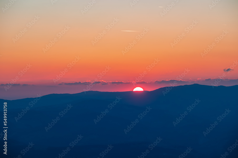 Scenic view of sun going up behind mountain Koralpe during sunrise seen from mountain peak Zingerle Kreuz, Saualpe, Lavanttal Alps, Carinthia, Austria, Europe. Soft red colored sky creating calm vibes