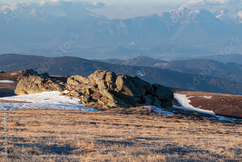 Scenic view of rock formation and Karawanks mountains at sunrise seen from alpine meadow at Ladinger Spitz, Saualpe, Lavanttal Alps, Carinthia, Austria, Europe. Early morning golden hour in Wolfsberg photo