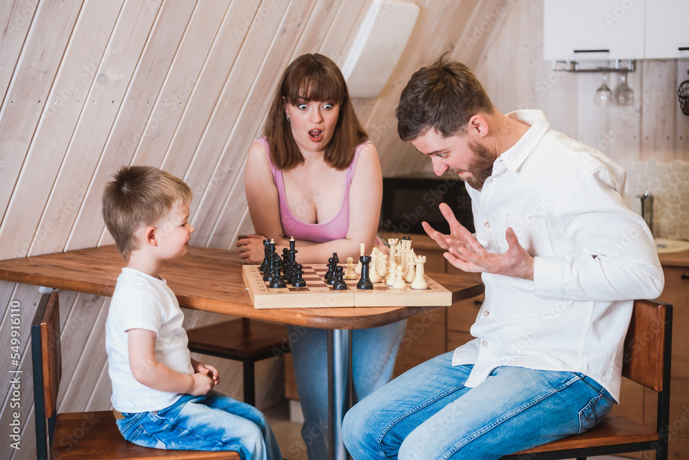 Happy family mother, dad and their son playing chess in the room Happy family mother, dad and their son playing chess in the room