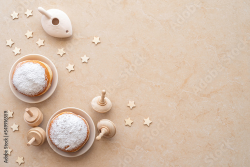 Traditional Hanukkah doughnut Sufganiyah, wooden spinning tops on marble background.