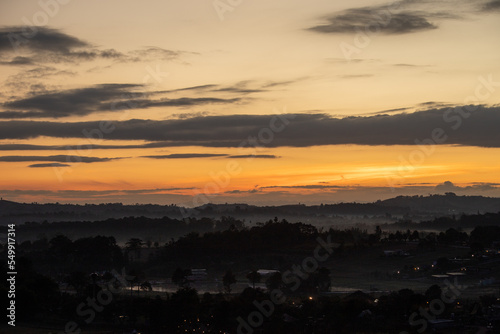Morning view at morning sunrise, clouds in orange crimson colors. Silhouettes of houses roofs, trees, and a monastery on the hill. Colorful scenery skyline background. © benjaean