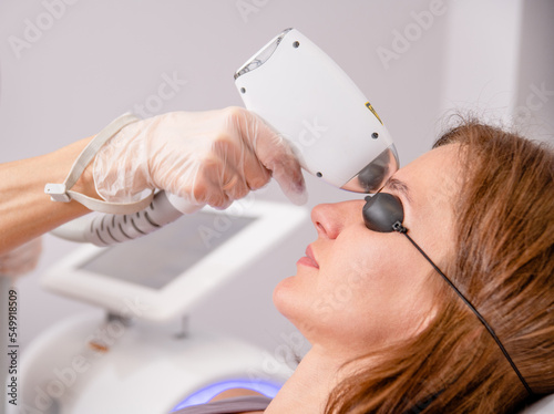 Professional beautician removes hair on the face of an young woman using a laser. Unibrow removal, laser procedure at clinic photo