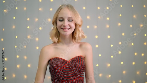 Blonde girl in a red dress adjusts her hair, smiles.
