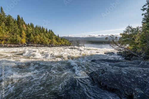 Famous waterfall Tannforsen northern Sweden, with a rainbow in the mist and rapid flowing cascades of water © CL-Medien