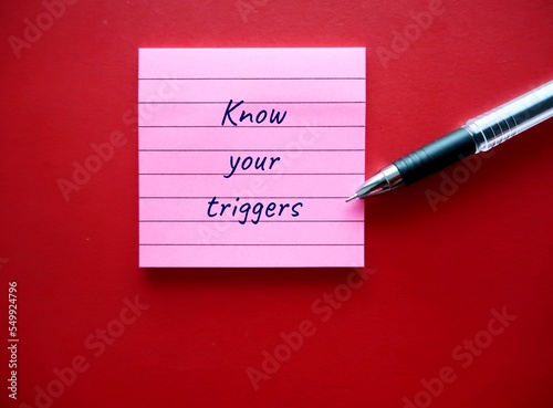 On red background, pen writing on note pad KNOW YOUR TRIGGERS, learning to know experience of having emotional reaction to a disturbing topic in the media or social setting and empower to cope with it