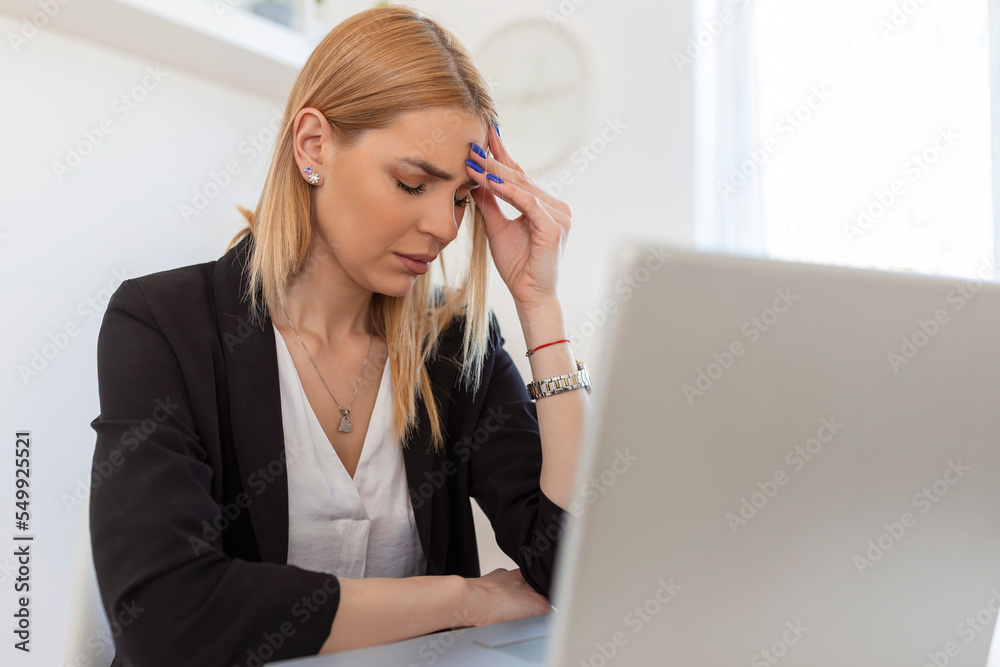 Young frustrated woman working at office desk in front of laptop suffering from chronic daily headaches. Feeling exhausted. Frustrated young woman looking exhausted while sitting at her working place Young frustrated woman working at office desk in front of laptop suffering from chronic daily headaches. Feeling exhausted. Frustrated young woman looking exhausted while sitting at her working place