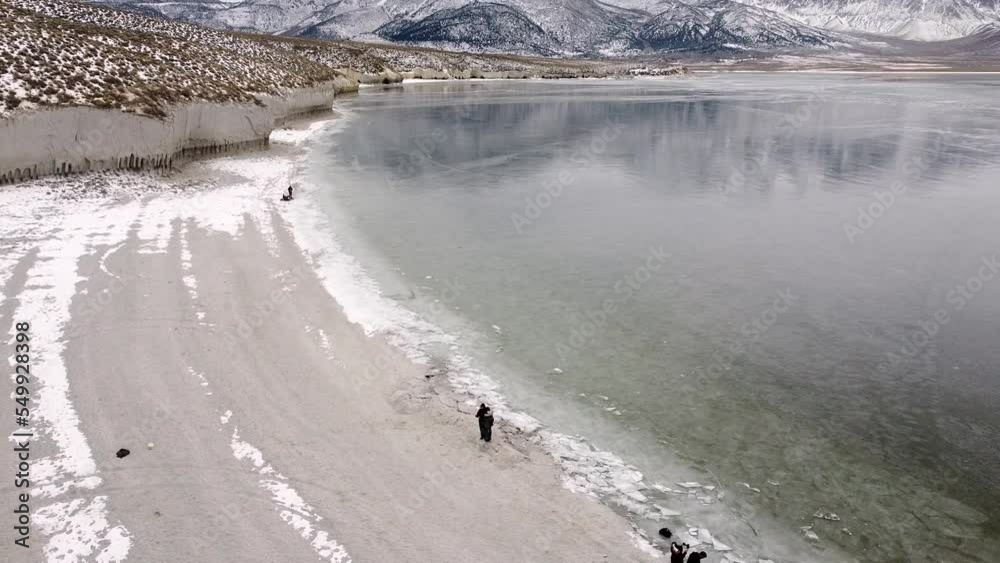 Drone circling around tourists standing near the shore of Crowley lake and revealing snow covered mountain range and reflection on lake water Drone circling around tourists standing near the shore of Crowley lake and revealing snow covered mountain range and reflection on lake water