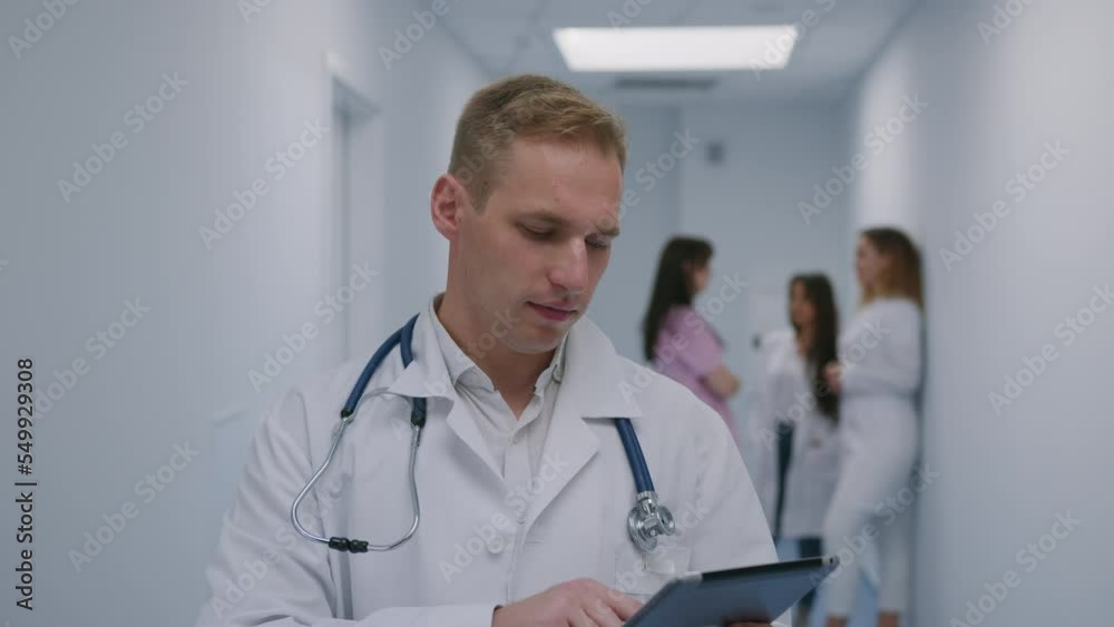 Portrait of a male doctor with a tablet on the background of a hallway of a modern clinic Portrait of a male doctor with a tablet on the background of a hallway of a modern clinic