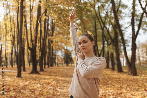 Serious female athlete warming up arms and exercising during fitness workout in autumn park 