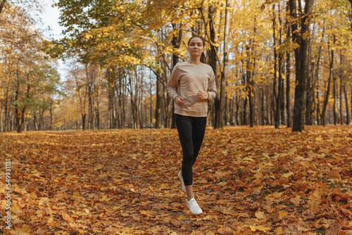 Full body of confident sporty female running during training in autumn park 