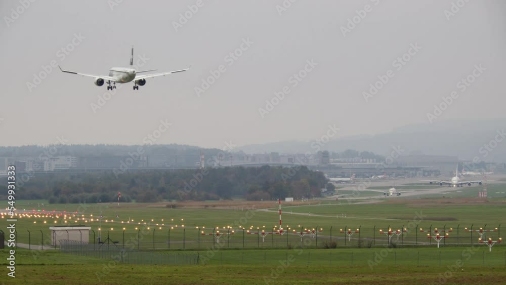 A passenger airplane is landing on a runway illuminated by lights, A380-800 is taxiing in the background A passenger airplane is landing on a runway illuminated by lights, A380-800 is taxiing in the background
