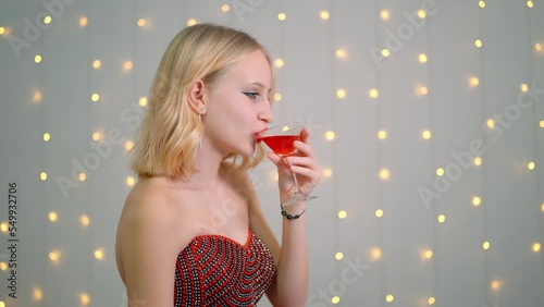 blonde drinks wine from a glass in a red dress.