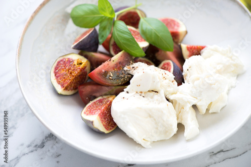 Close-up of tomato salad with fresh figs and mozzarella cheese in a beige plate, selective focus