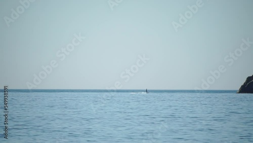 A motorized surfboard with a rider moving on a calm sea. The silhouette of a man on a water scooter glides through the water. Sports and sea activities on a beach holiday. Slow motion. photo